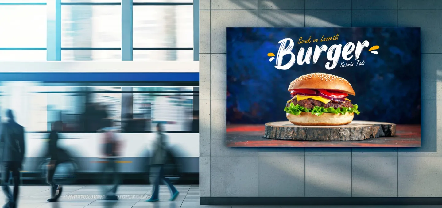 Bir metro istasyonundaki büyük bir reklamda, ahşap bir tahta üzerinde marul, domates, soğan ve peynirle birlikte sulu bir hamburger gösterilmekte, mavi bir arka plan üzerinde kalın harflerle "Burger" ve "Hayran Bırakmayı Arayın" ifadeleri yer almaktadır. Yakınlarda hareket halindeki insanlar ve bir tren bulanıklaştırılmış.
